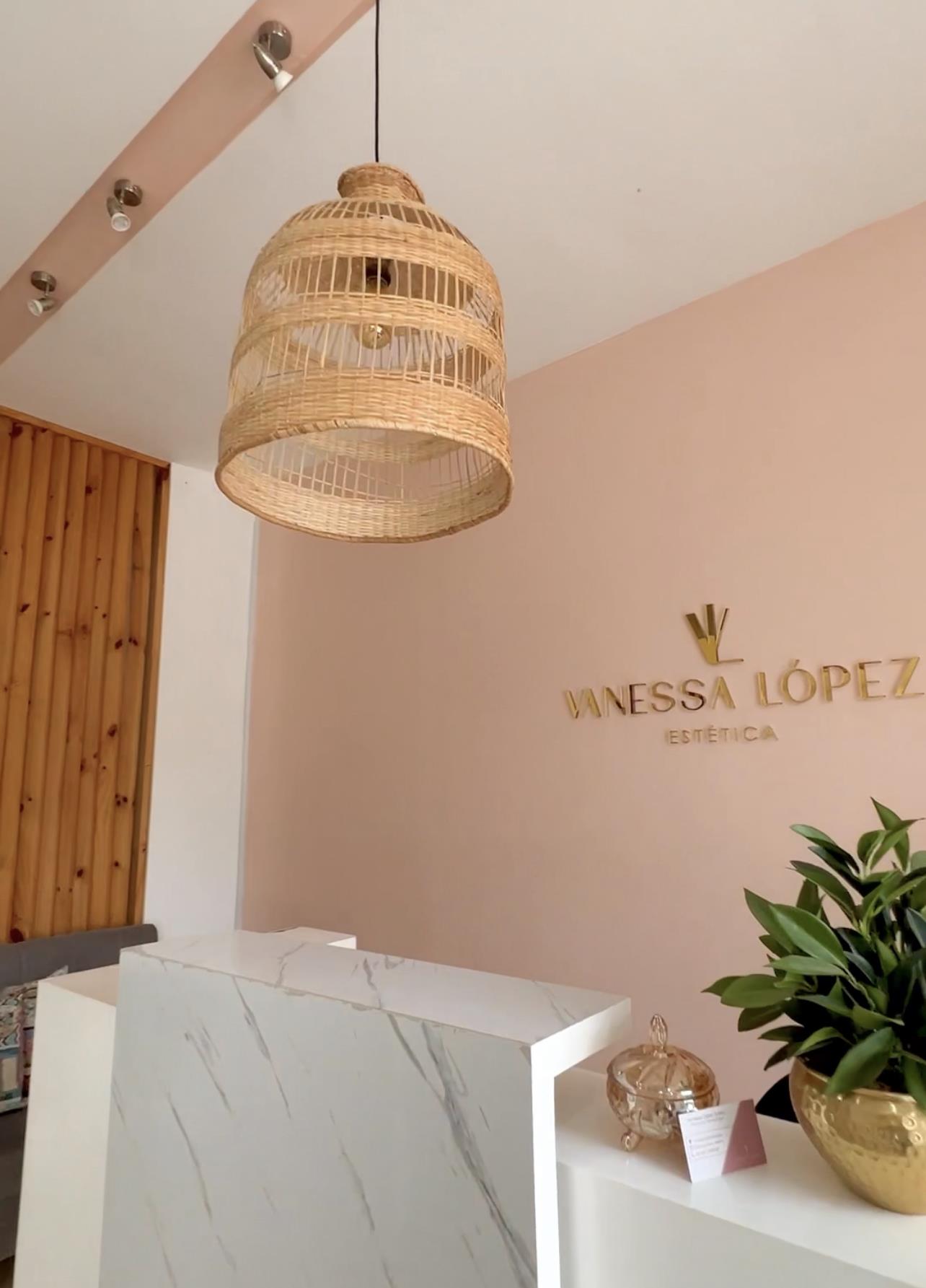 Recepción rosada con el letrero dorado de Vanessa López Estética y lámpara de mimbre